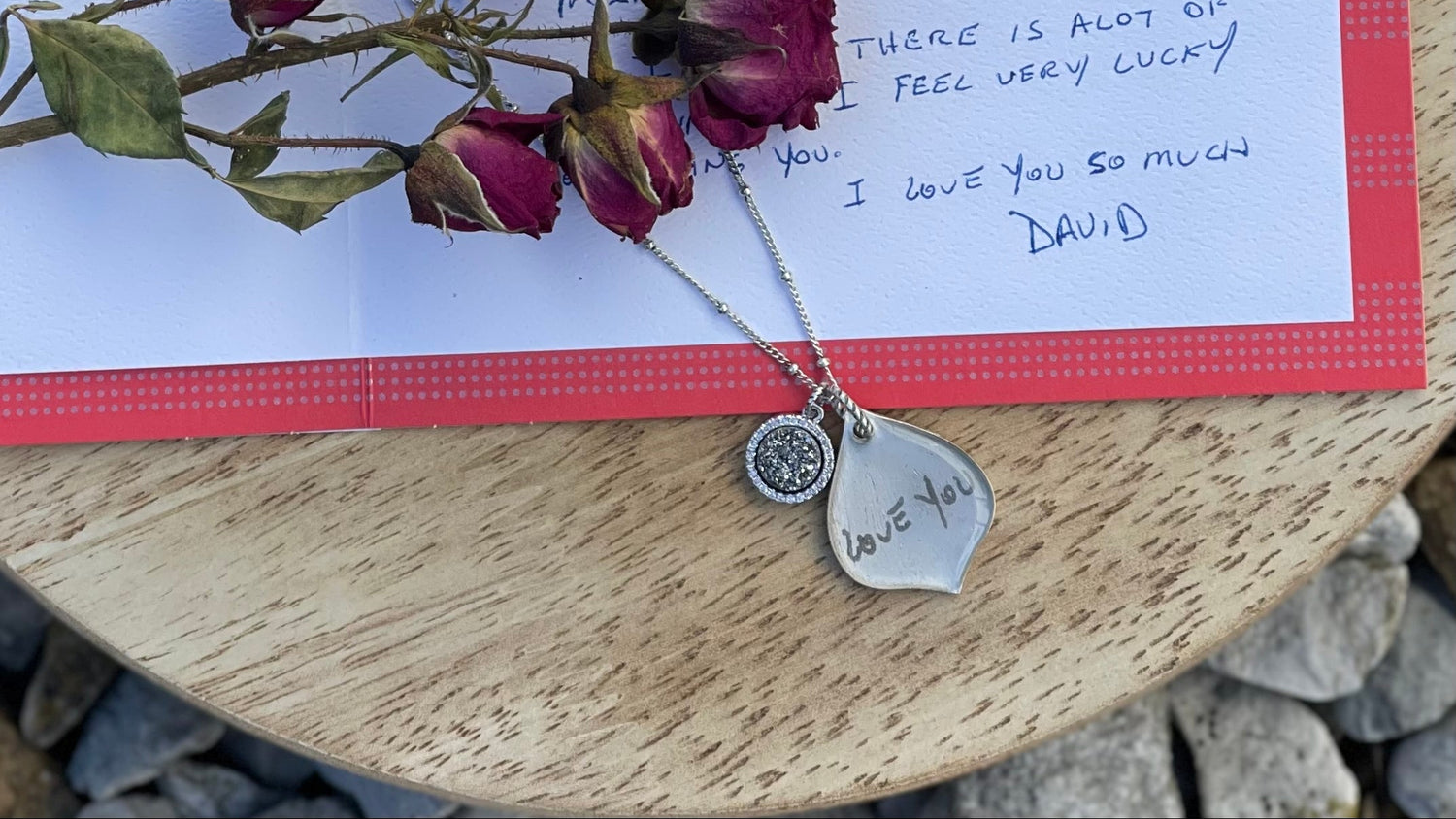 Valentine's Day card with a necklace and rose buds on a wooden surface